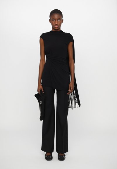 Top negro sin mangas con textura drapeada, combinado con pantalones anchos negros. Los accesorios incluyen un chal con flecos y un bolso texturizado.