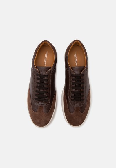 Paire de baskets décontractées en cuir et suède marron avec lacets noirs, semelles intérieures brandées et semelles en caoutchouc blanches, vues de dessus sur fond blanc.