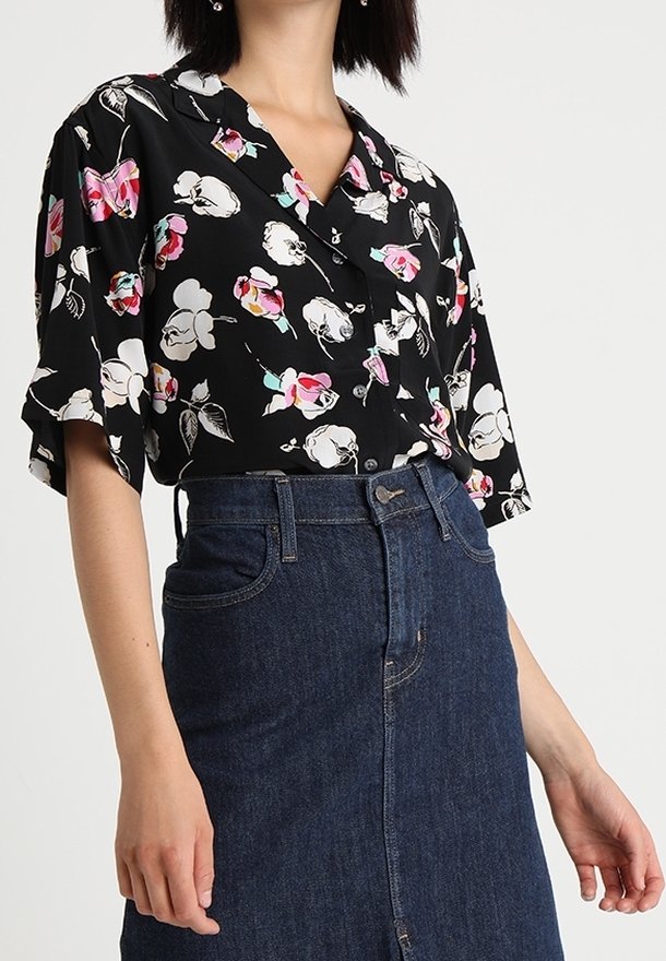 Femme portant un t-shirt noir à manches courtes avec un imprimé floral blanc et rose, rentré dans une jupe en jean bleu foncé taille haute.