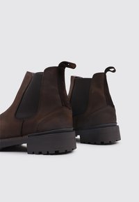 Bottes Chelsea en cuir marron avec des panneaux élastiques noirs sur les côtés, une languette de tirage en boucle et des semelles en caoutchouc noir robustes avec un motif de bande de roulement texturé.
