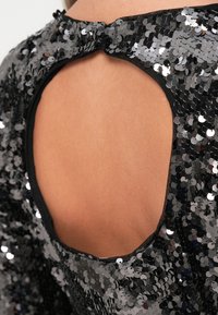 Μαύρο ύφασμα με παγιέτες με κυκλική κοπή στο πίσω μέρος του λαιμού, με λεπτό περιθώριο και μαλακή υφή, που αντανακλά το φως από πολλές γωνίες.