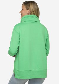 Sudadera verde de cuello alto con textura suave y bolsillo lateral con cremallera. Presenta un corte relajado y dobladillo acanalado.