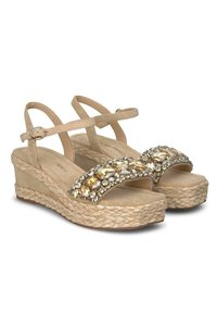 Sandalias de cuña beige con suela de yute trenzado, que presentan una tira adornada con piedras brillantes y una correa en el tobillo ajustable para un ajuste seguro.