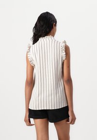 Top sans manches en lin beige clair avec des rayures verticales bleu marine, muni d'accents froncés aux épaules et d'un col haut.