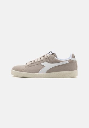Suede sneakers in beige with a white leather accent, flat rubber sole, and perforated detailing. Lace-up closure, minimalist design.