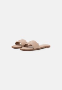 Beige sandaler med rund tå og brede, teksturerte stropper. Flat såle med en liten glans og preget logo på den øverste stroppen.