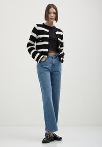 Cardigan a righe bianche e nere in maglia con apertura frontale, abbinato a jeans a vita alta blu chiaro e mocassini neri. Texture morbide.