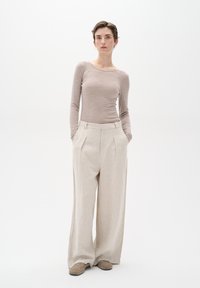 Top beige a maniche lunghe abbinato a pantaloni in lino a gamba larga e alta vita in una tonalità neutra chiara, con pieghe frontali e tasche laterali.