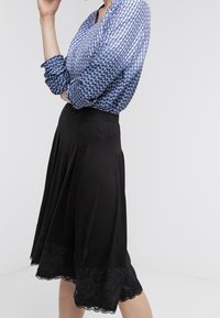 Blusa azul con estampado y mangas largas, combinada con una falda negra con un dobladillo de encaje. Tejido suave con un diseño acampanado.