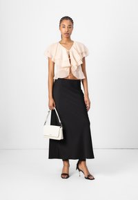 Blouse rose pâle à volants avec un lien à l'avant, jupe longue noire et talons noirs à lanières. Sac à main blanc au design structuré avec des accents en argent.