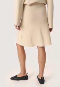 Beige knælang nederdel i et blødt, tekstureret stof med en udskåret kant. Kombineret med sorte, samlet ballerinaer.