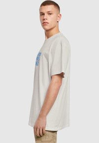 Lichtgrijze katoen T-shirt met korte mouwen, voorzien van blauwe tekst die over de voorkant is gedrukt. Ronde hals ontwerp, relaxed fit.