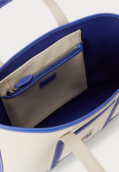 Bézs szövet bevásárlótáska kék részletekkel, belső zsebekkel és cipzáras rekesszel. Masszív fogantyúkkal és kontrasztos varrással rendelkezik.