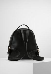 Czarny skórzany plecak o gładkiej fakturze, zaokrąglonym kształcie i regulowanych paskach. Złote elementy metalowe oraz minimalistyczny design.