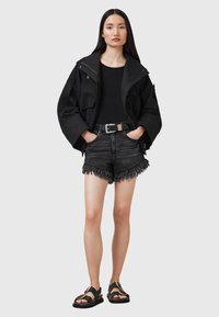 Giacca nera oversize, top nero aderente, pantaloni denim scuri con orlo sfrangiato e sandali neri con dettaglio in oro.