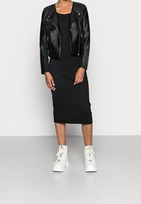 Abito midi nero a coste abbinato a una giacca di pelle nera attillata e sneakers alte bianche con accenti gialli e lacci.