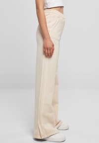 Lys beige vidde bukser med en myk tekstur, med elastisk midje og sidesøm detaljer, kombinert med hvite joggesko.