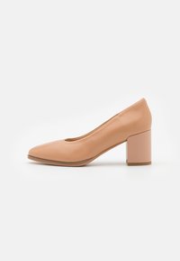 Escarpin à talon bloc en cuir nude avec un bout pointu et une texture lisse. Le design simple présente un col arrondi et des détails de couture minimaux.