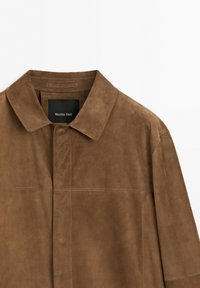 Veste en daim marron avec col et boutons dissimulés sur le devant, montrant la moitié supérieure et l'étiquette de la marque à l'intérieur du col.
