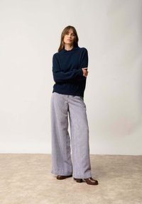 Granatowy sweter z dzianiny o luźnym kroju i szerokich mankietach, w połączeniu z paskowanymi spodniami o szerokich nogawkach w jasnych i ciemnych odcieniach oraz brązowymi, platformowymi obcasami.