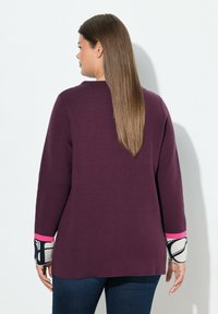 Maglione prugna con maniche lunghe e polsini con accenti rosa; presenta un design a fantasia e una texture morbida, abbinato a jeans scuri.