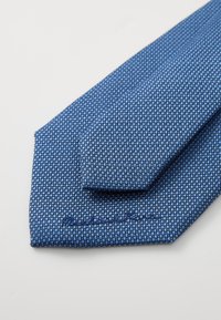 Teksturt blå slips med geometrisk mønster, som har en litt spiss tupp og broderte detaljer nær den brede enden.
