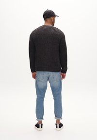 Donkergrijze gebreide trui met ribbeltextuur, lange mouwen en een ronde schouderontwerp, gecombineerd met lichtblauwe tapered jeans en zwarte sneakers.
