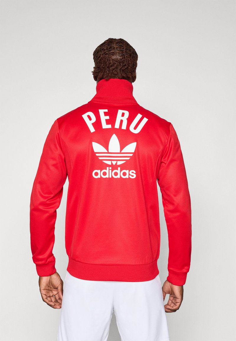 Sileda punane spordijope, mis on valmistatud siledast kangast. Omab kõrget krae, valget teksti sõnaga "PERU" ning Adidas'e logo koos kolme triibuga seljal.