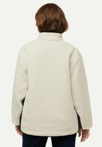 Giacca di pile bianca con colletto alto. Presenta una texture morbida, una vestibilità ampia e accenti neri a contrasto lungo i lati.