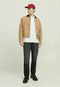 Beige jeansjacka med svart krage, vit t-shirt under, mörka jeans och svarta skor. Röd keps med vit logotyp.