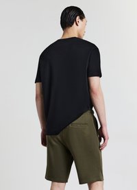 T-shirt nera a maniche corte con orlo leggermente più lungo sul retro, abbinata a pantaloncini verde oliva con tasca posteriore e vita elastica.