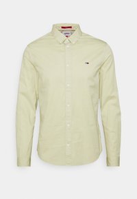Camicia a maniche lunghe color giallo chiaro in cotone, con colletto alla camicia e una piccola patch del logo sul lato sinistro del petto.
