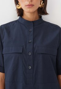 Navyblauschirt mit Stehkragen, kurzen Ärmeln und zwei Brusttaschen, ausgestattet mit einer Knopfleiste auf der Vorderseite. Aus glattem Baumwollstoff.