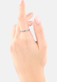 Una mano con las uñas bien cuidadas muestra un anillo de plata con pequeñas piedras de colores, contra un fondo simple.