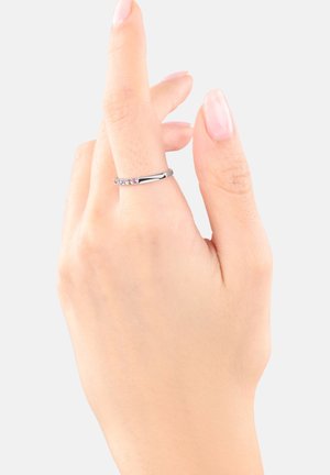 Una mano con las uñas bien cuidadas muestra un anillo de plata con pequeñas piedras de colores, contra un fondo simple.