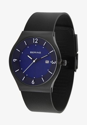 Schwarze Armbanduhr mit blauen Zifferblatt, weißen Stundenmarkierungen, Datumsanzeige auf 3 Uhr und schwarzem Mesh-Armband, die 10:10:39 anzeigt.