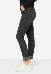 Jeans ajustados de denim gris oscuro con un dobladillo enrollado que presenta un detalle en negro con patrón. Combinados con zapatillas blancas.