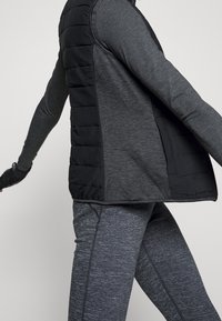 Svart pufferväst med en texturerad grå långärmad tröja och matchande grå leggings, med en figursydd design och kontrasterande material.