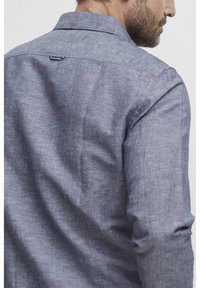 Camicia grigia in lino a maniche lunghe, con colletto classico, tessuto texturizzato e un accento ad anello sul retro del colletto.