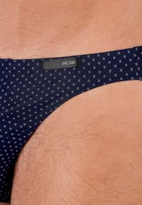 Marinblå herrsimbyxa med små vita prickar, med en svart etikett med varumärket "HOM" på midjebandet. Slät textur.
