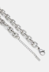 Collier en chaîne argentée chunky avec de grands maillons et un fermoir à pince de homard, comprenant une chaîne d'extension réglable avec une petite étiquette.