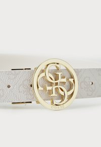 Ceinture blanche texturée avec une boucle circulaire dorée ornée des lettres entrelacées "G" et "C" et de gravures. Ajustable avec de petits clips en métal.