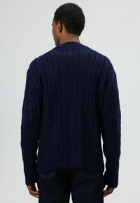 Marineblauer Strickpullover mit Zopfmuster, gerippten Bündchen und Saum sowie einem Rundhalsausschnitt. Die Textur ist dick und grob.