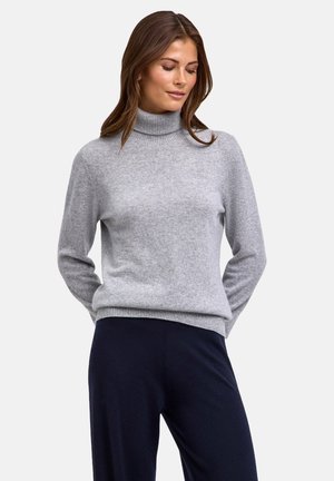 Pull à col roulé gris clair en tissu doux. Présente des manches longues et une bordure côtelée. Assorti à un pantalon de couleur foncée.