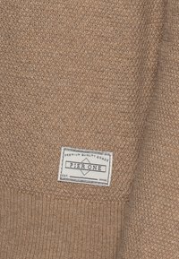 Ruskea neulottu villapaita, jossa on resorireunus hihansuissa ja etiketti, jossa lukee "Pier One" ja jossa on timantin kuva. Pinta on pehmeä ja siinä on kudottu kuvio.