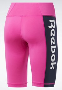 Shorts de sport roses avec un panneau latéral noir comportant le logo blanc Reebok en vertical.