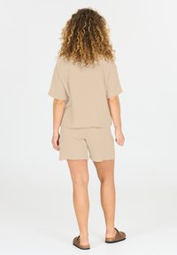 Beige twee-delige outfit met een losse, kortslobige top en bijpassende shorts, gemaakt van textuurstof. Sandalen maken de look af.