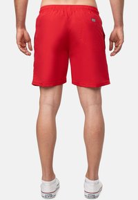 Pantaloni corti rossi realizzati in materiale leggero, con elastico in vita, tasca posteriori e orlo cucito. Indossati con sneakers bianche.