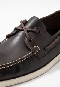 Braune Lederbootsschuhe mit schwarzen Ösen und braunen Schnürsenkeln. Ausgestattet mit beigen Nähten und einer Gummisohle mit strukturiertem Rand.