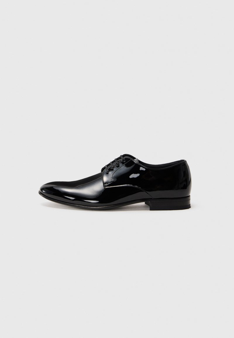 Zapato de vestir para hombre de piel negra pulida con cordones y tacón bajo, sobre un fondo gris claro liso.